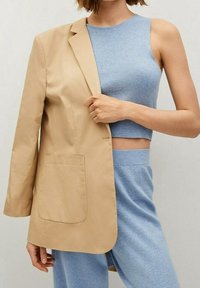 Blazer beige de corte holgado con un bolsillo, superpuesto a un top corto sin mangas de color azul claro. Tejidos texturizados en un ajuste relajado.