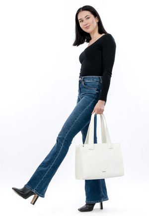 Un sac fourre-tout en cuir blanc avec une surface texturée et deux poignées solides, assorti à un jean évasé taille haute bleu foncé et des bottes noires à talons.