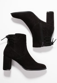 Paio di stivaletti neri in suede con tacco a blocco, zip laterali e dettaglio di lacci sul retro, mostrati da viste laterale e superiore.