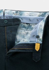 Pantalons en tissu texturé sombre avec une doublure intérieure à motif bleu, une fermeture éclair dorée et un accent beige. Comprend un bouton rond et un détail de marque.