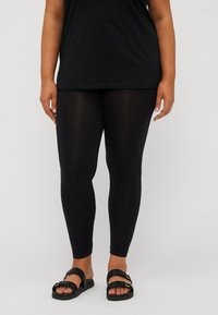 Black leggings made of stretchy fabric, featuring a smooth texture and a fitted design, paired with black sandals with two straps and gold accents.