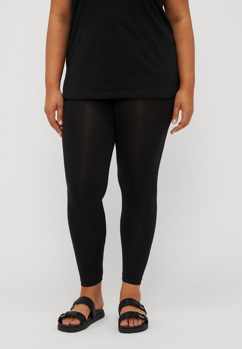 Black leggings made of stretchy fabric, featuring a smooth texture and a fitted design, paired with black sandals with two straps and gold accents.