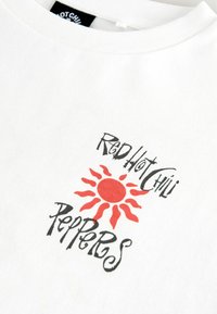 Hvid bomulds t-shirt med sort stiliseret tekst "Red Hot Chili Peppers" og et centralt rødt solgrafik med spidse stråler.