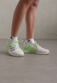White and light green athletic shoes with mesh and synthetic material, featuring a textured heel and three gray stripes on the side.