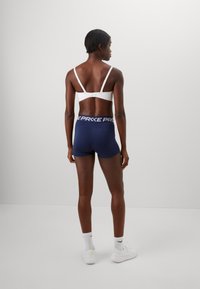 Hvid sports-bh og marineblå shorts med logo på taljen. Shortsene er tætsiddende, med en glat tekstur og minimale sømme.
