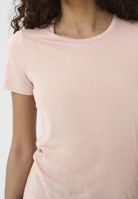 Light pink t-shirt with a soft texture, round neckline, and short sleeves. Smooth fabric with minimal stitching details.