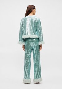 Conjunto em duas peças em azul aqua com paetês, apresentando uma jaqueta cropped com acabamento em pelo sintético e calças de perna larga combinando, ambas cintilantes com uma textura brilhante.