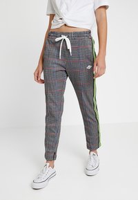 Zwart-witte geruite joggerbroek met rode en blauwe lijnen, voorzien van een witte trekkoord en neon groene zijstrepen. Gecombineerd met witte sneakers.