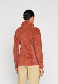 Fleece dukserica s kapuljačom u boji opečnjak s teksturiranom, rebrastom prednjom stranom i glatkom stražnjom panelom. Ima usku kapuljaču i prilagođene rukave.