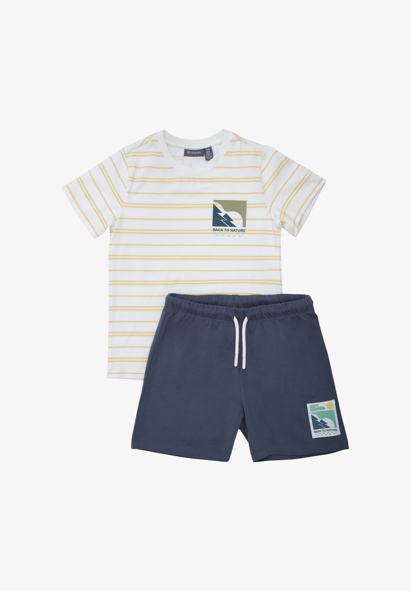 Camiseta blanca de manga corta con finas rayas amarillas y pantalones cortos azul marino, ambos con parches gráficos que dicen "Volver a la naturaleza".