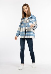 Blauw en grijs geruite spijkerjas met grote knopen en twee borstzakken, gedragen over een witte top en gecombineerd met donkere jeans en witte sneakers.
