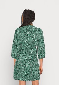 Vihreä kukkakuvioitu mekko, jossa on vyötärö korostettu, puolipitkät hihat ja rento istuvuus. Materiaali vaikuttaa kevyeltä ja teksturoidulta.