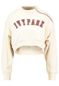 Krátká krémová mikina s nápisem "IVYPARK" červenou barvou. Má žebrovaný límec a manžety, na jednom rameni patentky a červený akcent.