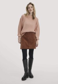 Rosa geripptes Sweatshirt, brauner Cordrock, schwarze Stiefeletten bis zum Knöchel, getragen mit schwarzen Strumpfhosen. Einfaches Design und strukturierte Materialien.