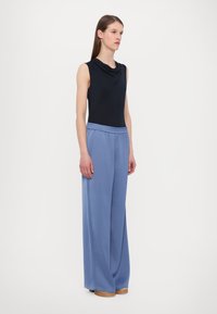 Top nero senza maniche con scollo drappeggiato, abbinato a pantaloni a gamba larga blu chiaro con vita elastica e tessuto morbido.