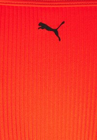 Tecido ribado vermelho com um logótipo preto da Puma. A textura parece suave com padrões verticais e um design ajustado.