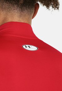 Rød sportstrøje med høj krave, lavet af glat stof. Har et sort cirkulært logo på ryggen nær nakkeområdet.