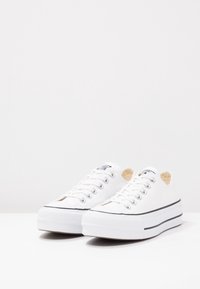 Sneaker bianche in tela con suola a piattaforma, punta rotonda, striscia nera decorativa e occhielli metallici, dotate di suola in gomma testurizzata.