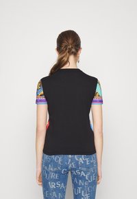 Top nero a maniche corte con maniche a fantasia colorata. Presenta un collo rotondo e una texture liscia. Abbinato a jeans in denim blu con stampa di testo.