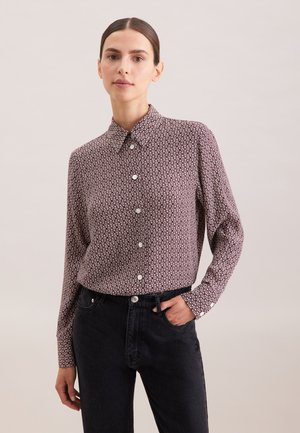 Camicia a maniche lunghe in bordeaux con un motivo geometrico, colletto a bottoni e bottoni sul davanti; abbinata a jeans neri scuri.