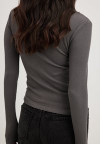 Grå ribbad långärmad topp sedd bakifrån, med en figurnära design. Matchad med högmidjade svarta jeans.