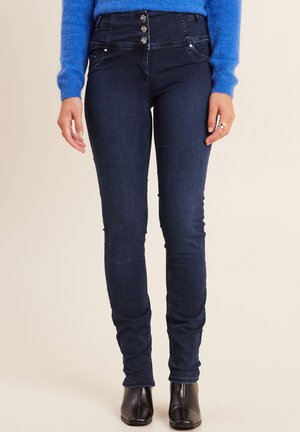 Dunkelblaue Skinny-Jeans mit hoher Taille, versehen mit drei Knopfverschlüssen und Fronttaschen, kombiniert mit schwarzen Knöchelstiefeln.