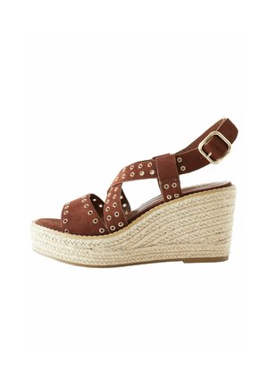 Sandal in suede marrone con zeppa, presenta fasce a taglio con borchie dorate, una suola intermedia in corda intrecciata e una cinghia alla caviglia regolabile con fibbia.