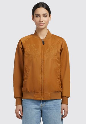 Giubbotto bomber bronzo con ricamo floreale sul petto, colletto e polsini a coste, e tasche laterali, abbinato a jeans azzurri chiari.