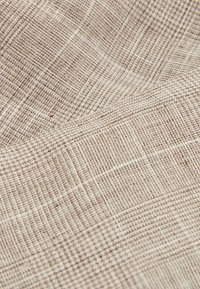 Beige texturerad tyg med ett rutmönster, med vävda detaljer och en mjuk, subtil lyster. Idealisk för möbelklädsel eller klädmaterial.