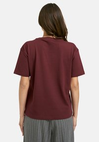 Burgundy t-shirt with a relaxed fit, short sleeves, and a crew neckline, paired with gray-striped trousers, smooth cotton texture.