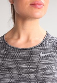 Top deportivo negro y gris con un patrón texturizado, escote redondo y un pequeño logo gris de Nike en el pecho.