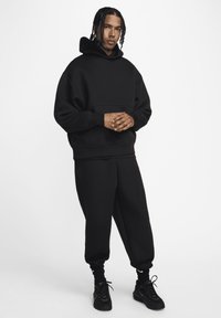 Sort bomuld oversized hoodie med en frontlomme, parret med matchende sorte sweatpants, der har ribbede manchetter og en afslappet pasform. Sorte sneakers.