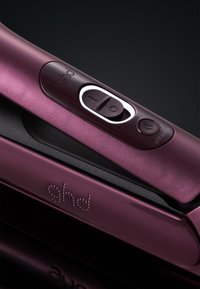 Le lisseur de cheveux GHD en finition violet métallisé présente un design épuré avec des boutons sur le manche et une surface texturée. Le logo est visible sur le côté.