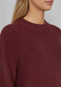 Burgundowa dzianinowa sweter z żeberkowaną teksturą, okrągłym dekoltem i subtelnie ukośnymi szwami na ramionach.