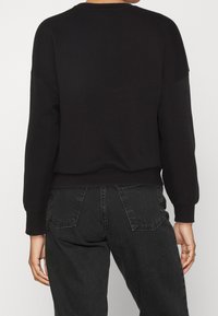 Musta collegepaita, jossa on rento istuvuus, pyöreä kaulus ja resorireunus. Sileä pinta. Yhdistetty tummanharmaisiin farkkuihin, joissa on takataskut.