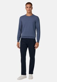 Hele sinises toonis pikkade varrukatega kampsun, ümmargune kaelus, koos tume siniste pükste ja valgete tossudega. Sile tekstuur, istuv disain, põhielemendid.