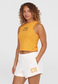 Żółty bawełniany crop top z czarnym napisem "KOBIETY FALI" oraz białe bawełniane szorty z podobnym napisem w kolorze pomarańczowym. Szorty mają elastyczny pas.