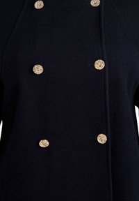 Navy blue coat with a textured fabric featuring five gold-tone decorative buttons and vertical stitching details along the front.