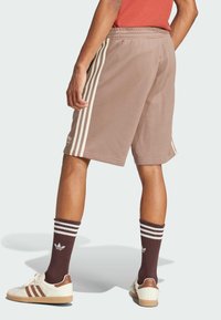 Shorts de sport marron avec des bandes blanches sur les côtés, associés à des chaussettes rayées marron et blanc, et des baskets marron et blanc.