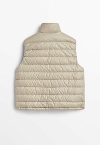 Beżowa pikowana kamizelka z wysokim kołnierzem, przeszywanym wzorem i bocznymi otworami. Materiał wydaje się gładki i lekki, odpowiedni do noszenia warstwowego.