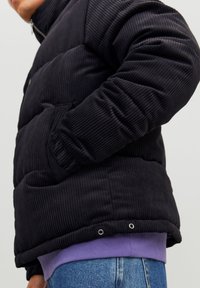 Czarna pikowana kurtka sztruksowa z pionowym prążkowaniem, bocznymi kieszeniami oraz widoczną pod spodem fioletową koszulą. Posiada zapięcie na zatrzaski u dołu.