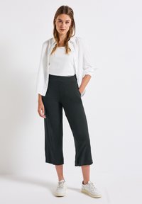 Svarta korta byxor med en bred bendesign, i kombination med en vit topp och vita sneakers. Outfiten har en avslappnad, lager-på-lager look.