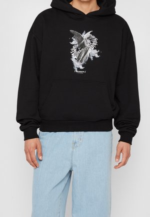Sudadera negra con un gráfico frontal que presenta un ángel emergiendo de las nubes. Material de algodón, bolsillo canguro, puños y dobladillo acanalados.