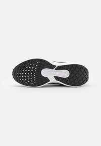 Semelle de sneaker noire et blanche présentant une surface en caoutchouc texturé pour une meilleure adhérence, avec une découpe centrale et des détails de marque.