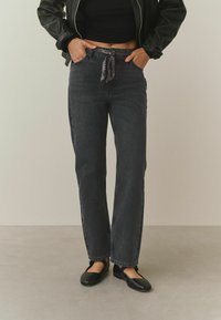 Čierne riflové nohavice s voľným strihom, s pásom so vzorovaným šnúrkou, bočnými vreckami a mierne ošúchanými lemami. Kombinované s čiernymi plochými topánkami.