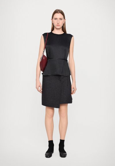 Čierny peplum top s hladkým textúrou, doplnený o sukňu po kolená v tmavosivej farbe so šikmým strihom a detailom gombíka. Červená kabelka na rameno.