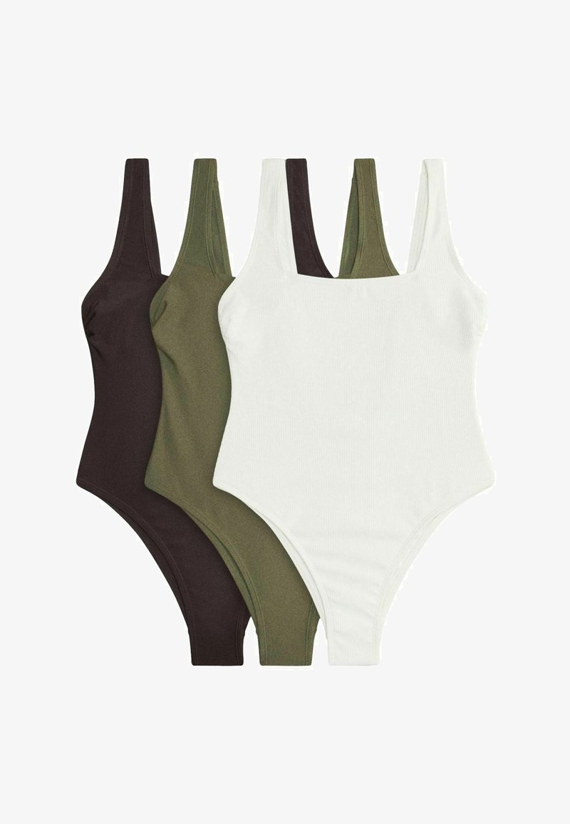 Trois débardeurs côtelés noir, vert olive et blanc, disposés en chevauchement sur un fond blanc.