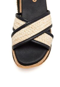 Sandal platform in paglia intrecciata nera presenta cinghie incrociate, superficie testurizzata e una base nera ampia e liscia.