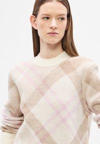 Hele beež värvi kampsun roosa ja pruuni ruudulise mustriga, millel on soonikuline kreemikas ümara kaelusega ja tekstureeritud kudumkangas.