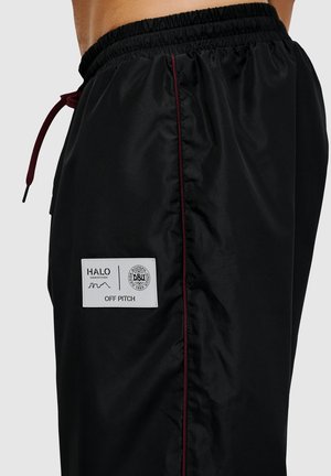 Black sports shorts with a glossy finish. Features a maroon side stripe and a white label with logos. Elastic waistband with drawstring.